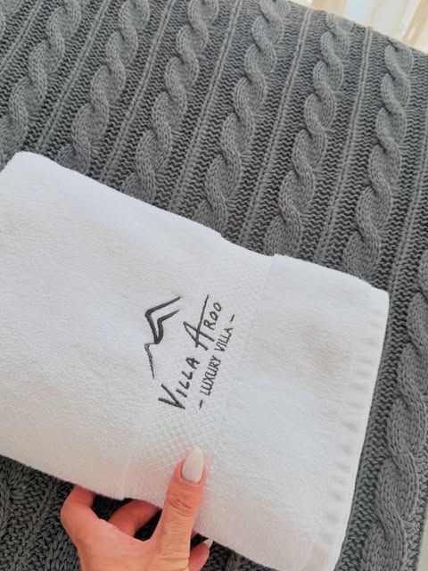 Peshqir i bardhë me qëndisjen Villa Aroo Luxury Villa mbi batanije të thurur